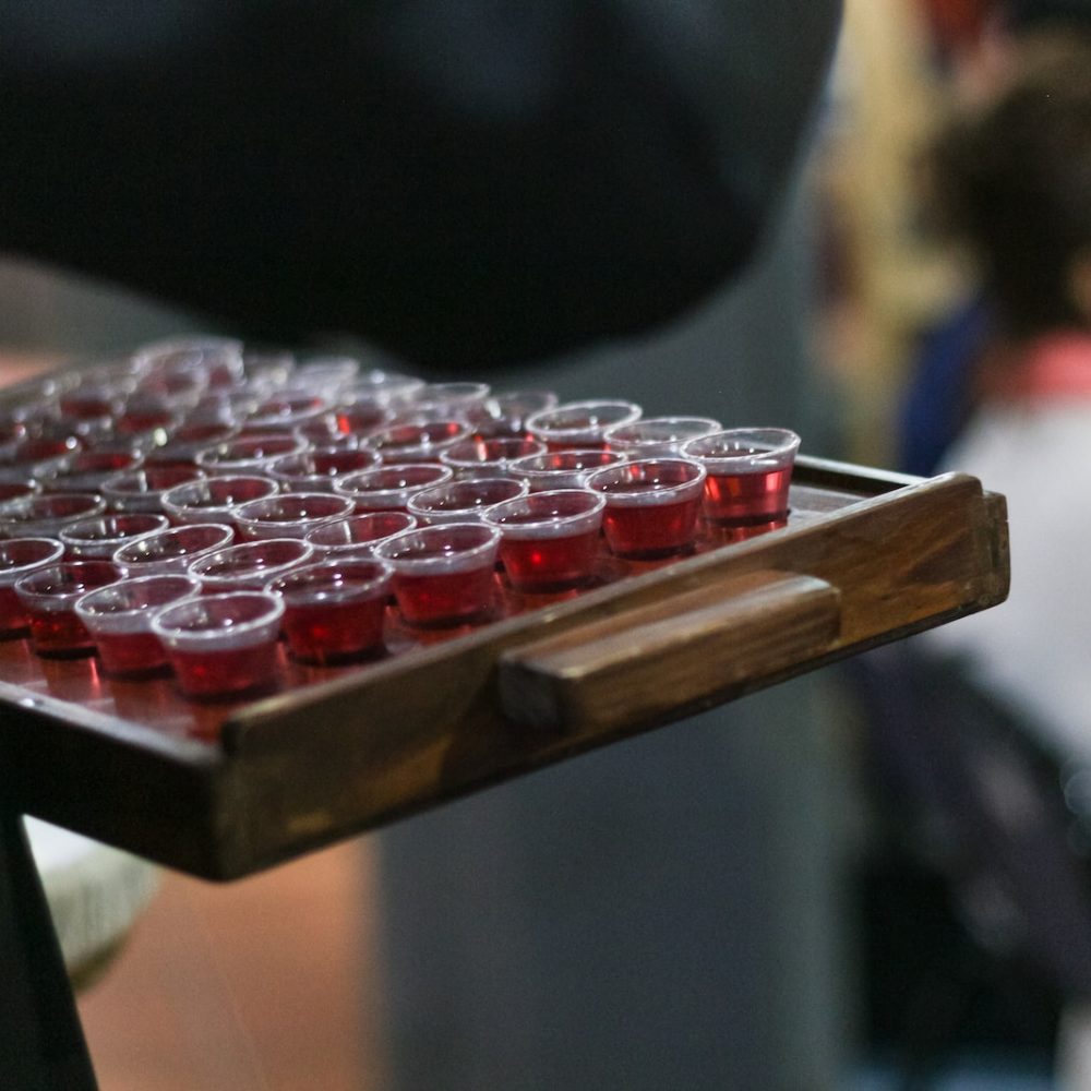person carrying red liquid filled mini disposable cups on wooden tray